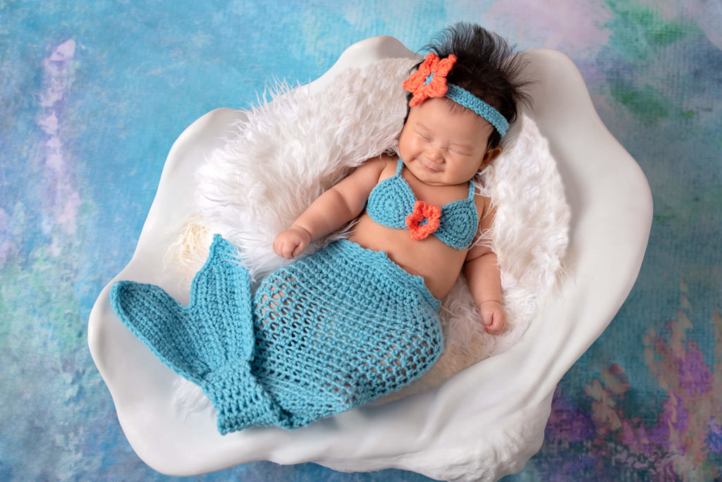 Laughing 100 days baby lying on seashell in crocheted mermaid outfit